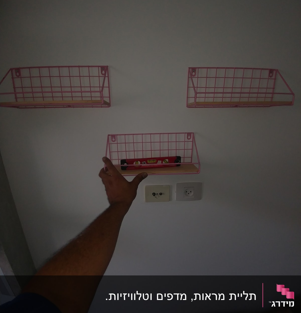 יד מתקינה מדף מתכת ורוד על קיר לבן